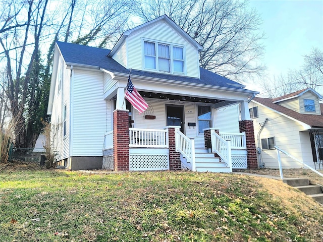 view of front of property featuring covered porch, a shingled roof, and a front yard