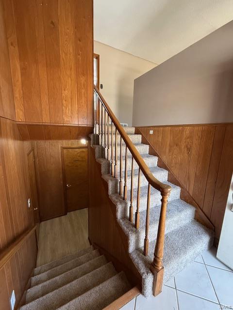 staircase featuring wood walls, wainscoting, and tile patterned floors