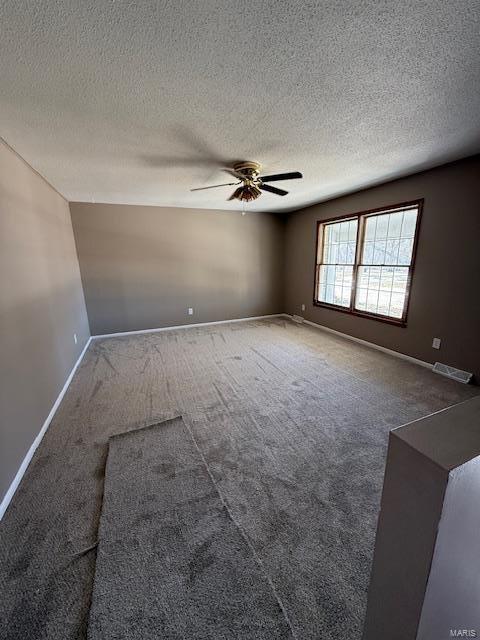 carpeted spare room with a ceiling fan, visible vents, a textured ceiling, and baseboards