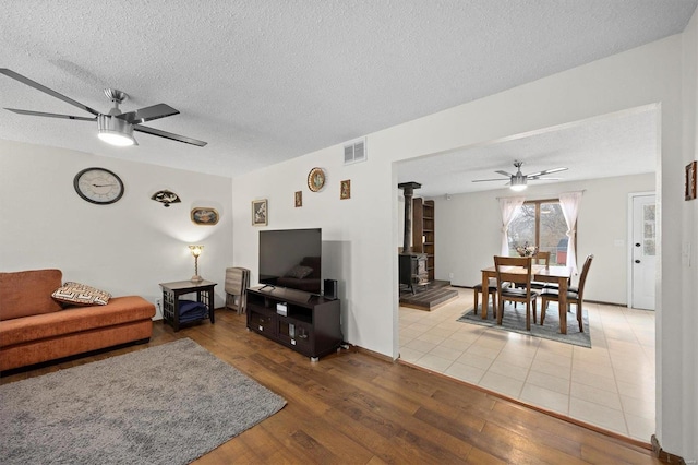 living area featuring a wood stove, wood finished floors, visible vents, and a ceiling fan