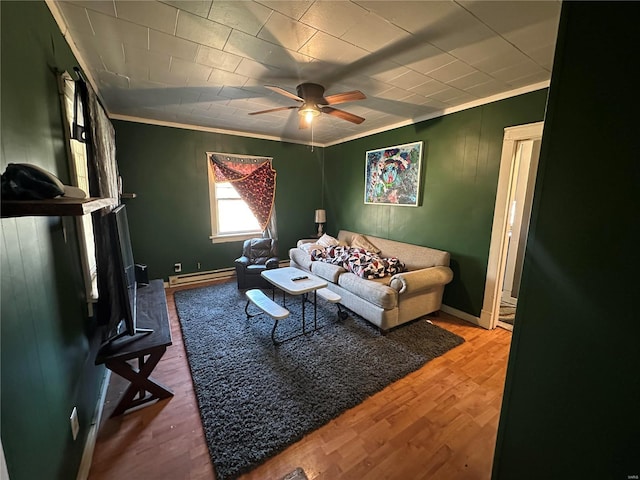 living room with a baseboard radiator, wood finished floors, a ceiling fan, baseboards, and ornamental molding