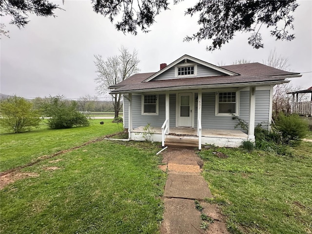 bungalow-style home featuring a shingled roof, a front lawn, covered porch, and a chimney