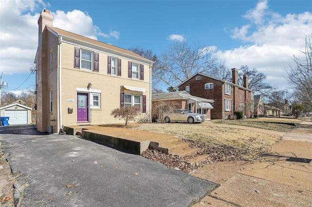 view of front facade with a garage, brick siding, an outdoor structure, driveway, and a chimney