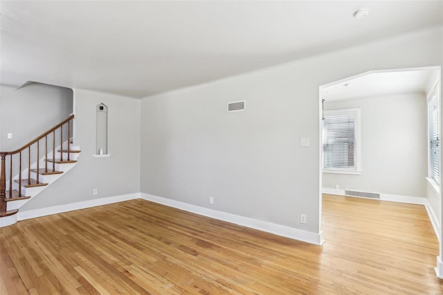 empty room with light wood-type flooring, visible vents, baseboards, and stairs
