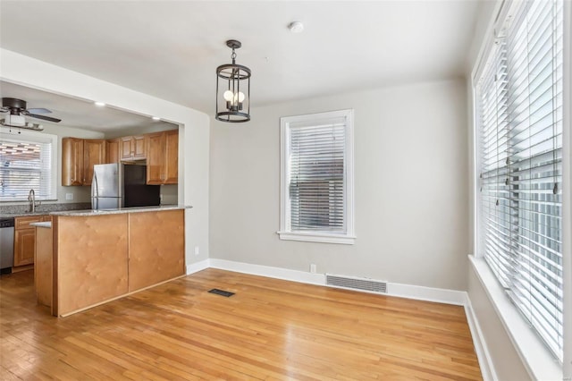 kitchen with light wood finished floors, visible vents, dishwasher, freestanding refrigerator, and ceiling fan with notable chandelier