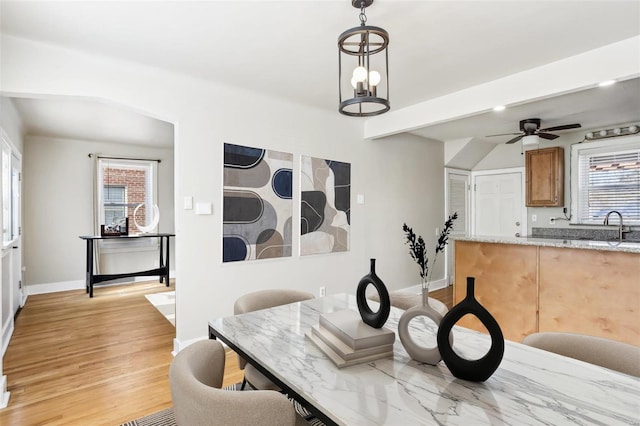 dining room with light wood-style flooring, baseboards, and ceiling fan with notable chandelier