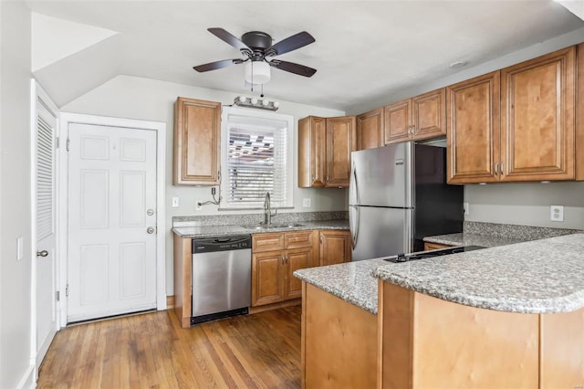 kitchen with stainless steel appliances, a peninsula, wood finished floors, a sink, and brown cabinets