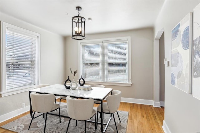 dining space with light wood-type flooring, baseboards, and a notable chandelier