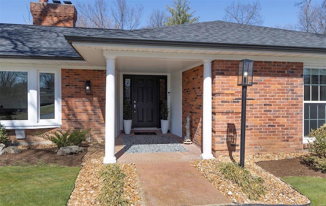 doorway to property featuring a shingled roof, brick siding, and a chimney