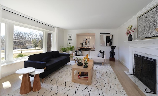 living room featuring crown molding, a fireplace, wood finished floors, baseboards, and an inviting chandelier