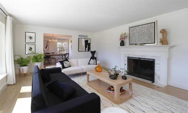 living area featuring light wood finished floors, a premium fireplace, ornamental molding, and a chandelier