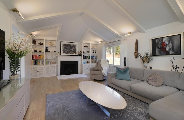 living room featuring a fireplace with raised hearth, vaulted ceiling with beams, built in shelves, and light wood-style floors