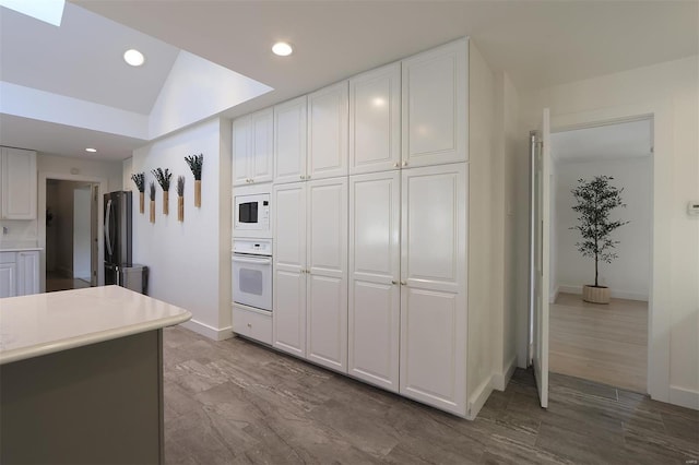 kitchen featuring recessed lighting, light countertops, white cabinets, white appliances, and baseboards