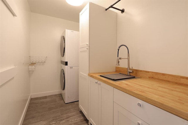 washroom with a sink, stacked washer and dryer, baseboards, and cabinet space