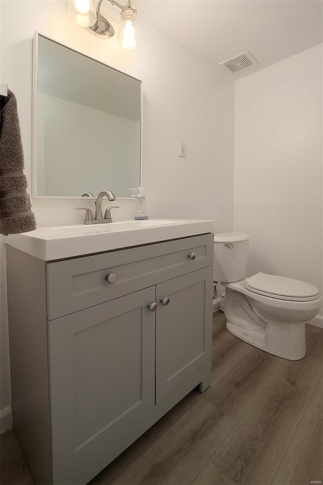 half bath with visible vents, vanity, wood finished floors, and toilet