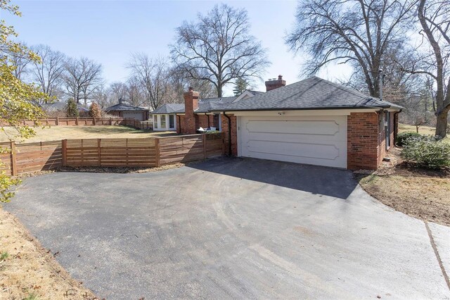 exterior space with brick siding, driveway, a chimney, and fence