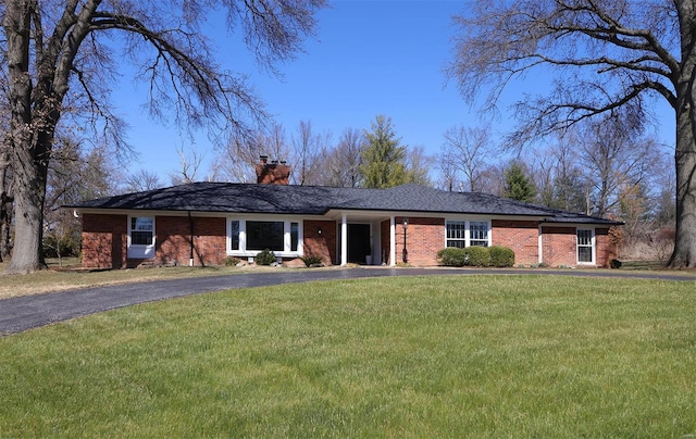 ranch-style home featuring aphalt driveway, a chimney, a front lawn, and brick siding