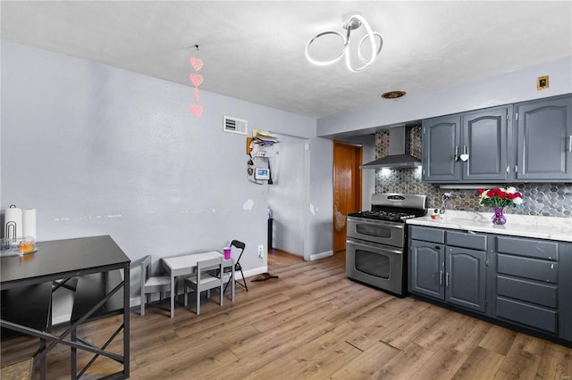 kitchen with light countertops, visible vents, backsplash, wall chimney range hood, and double oven range