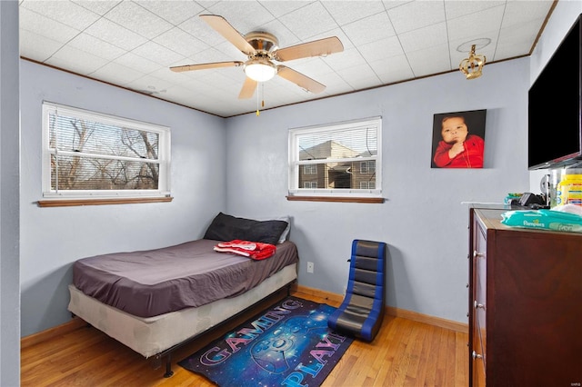 bedroom featuring ceiling fan, ornamental molding, wood finished floors, and baseboards