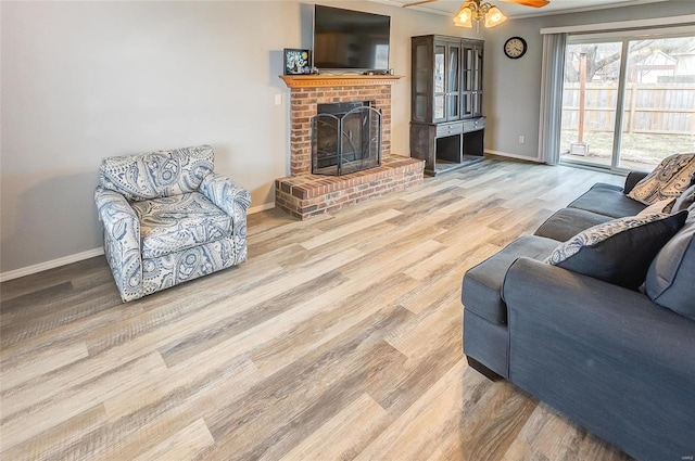 living area with a ceiling fan, a fireplace, baseboards, and wood finished floors