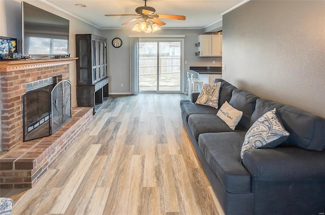 living room with ornamental molding, a brick fireplace, light wood-style flooring, and baseboards