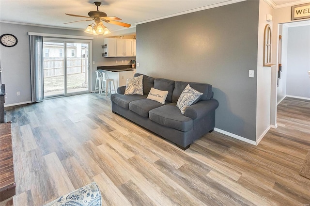 living room with a ceiling fan, baseboards, ornamental molding, and wood finished floors