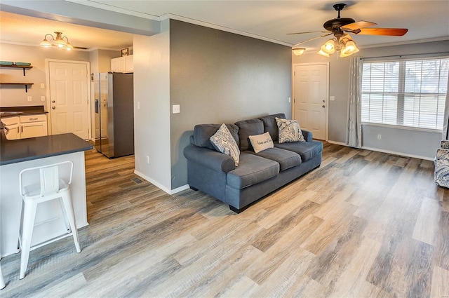 living area featuring ornamental molding, wood finished floors, a ceiling fan, and baseboards