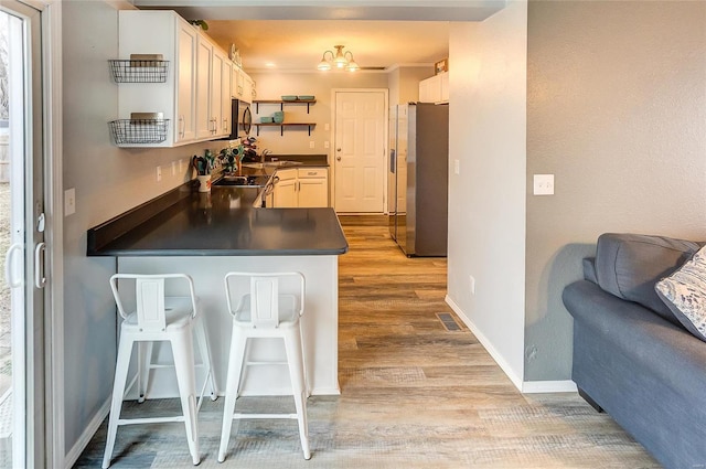 kitchen featuring stainless steel appliances, a peninsula, a kitchen breakfast bar, light wood finished floors, and dark countertops