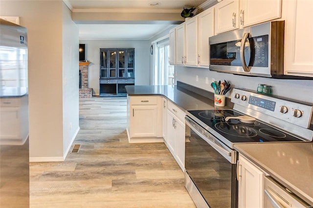 kitchen with light wood finished floors, stainless steel appliances, ornamental molding, and white cabinets