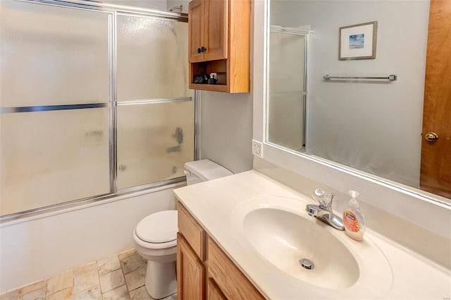 full bath with toilet, stone finish flooring, enclosed tub / shower combo, and vanity