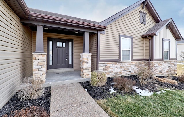 view of exterior entry featuring stone siding, roof with shingles, and covered porch