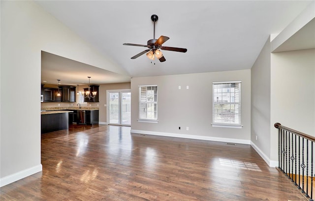 unfurnished living room featuring lofted ceiling, dark wood-style flooring, baseboards, and ceiling fan with notable chandelier