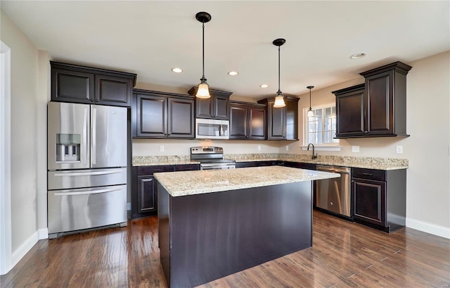 kitchen with dark wood-style floors, a kitchen island, appliances with stainless steel finishes, hanging light fixtures, and light stone countertops