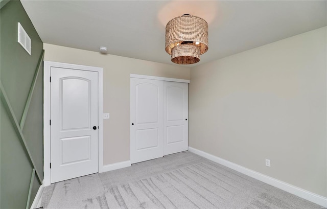 unfurnished bedroom featuring baseboards, visible vents, carpet flooring, a chandelier, and a closet