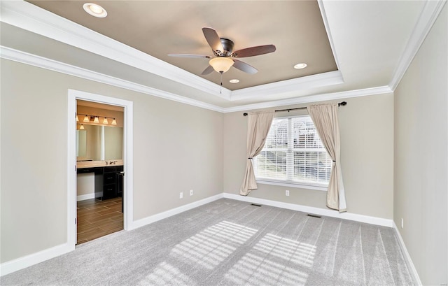 unfurnished bedroom featuring carpet flooring, visible vents, baseboards, ornamental molding, and a raised ceiling