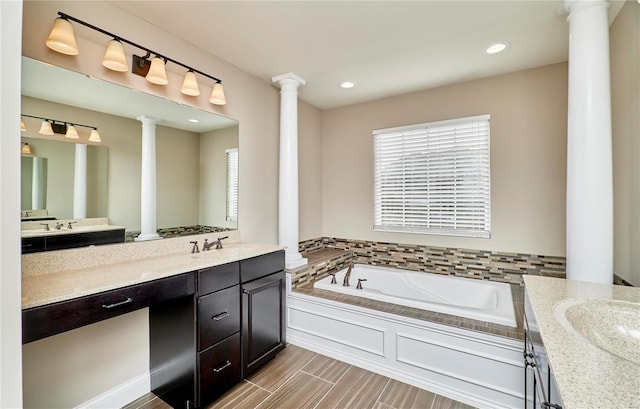 full bathroom with a sink, two vanities, a bath, and ornate columns