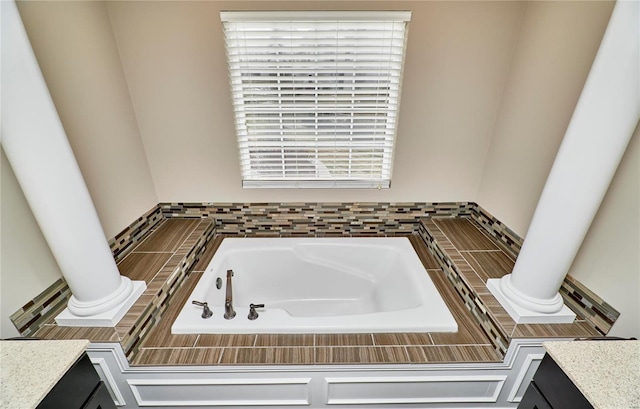 full bathroom featuring a garden tub, decorative columns, and vanity