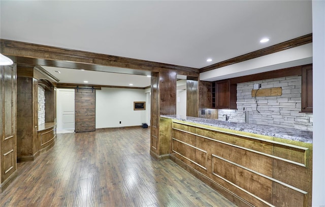 kitchen with a barn door, baseboards, decorative backsplash, dark wood-style floors, and crown molding