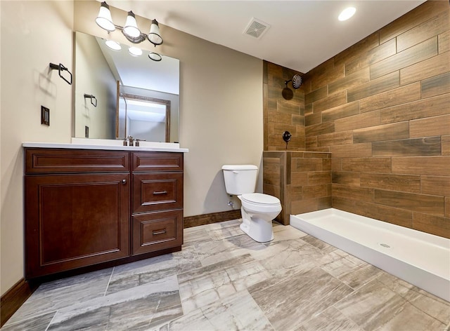 bathroom with visible vents, toilet, vanity, tiled shower, and baseboards