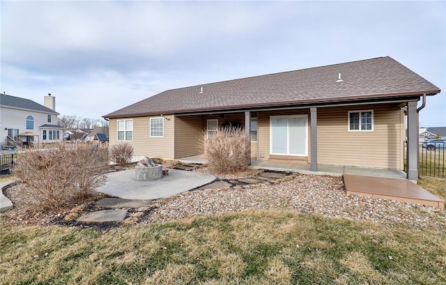 rear view of property featuring a patio area, a shingled roof, fence, and a fire pit