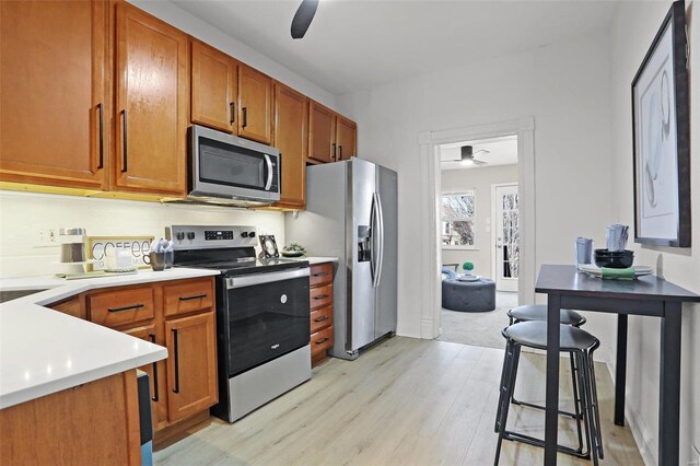 kitchen with light wood finished floors, brown cabinetry, a ceiling fan, stainless steel appliances, and light countertops