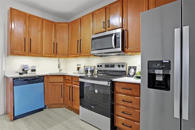 kitchen featuring light countertops, decorative backsplash, appliances with stainless steel finishes, light wood-style floors, and a sink