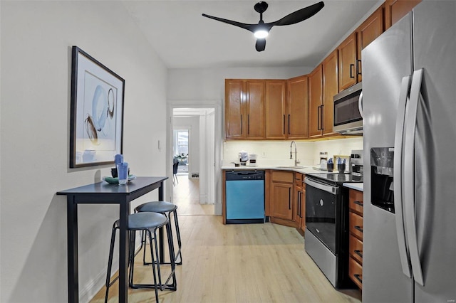 kitchen with light wood finished floors, stainless steel appliances, light countertops, a ceiling fan, and a sink