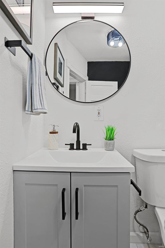 half bathroom with toilet, a textured wall, and vanity