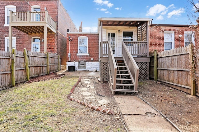 rear view of property with a yard, a fenced backyard, brick siding, and stairway