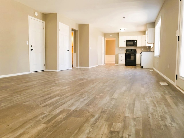 unfurnished living room with light wood-type flooring, a sink, and baseboards