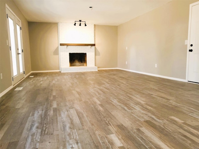 unfurnished living room with visible vents, baseboards, wood finished floors, a brick fireplace, and track lighting