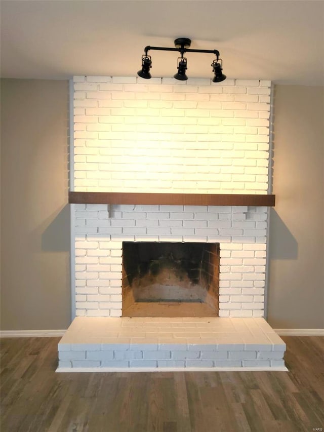 room details featuring a brick fireplace, baseboards, and wood finished floors