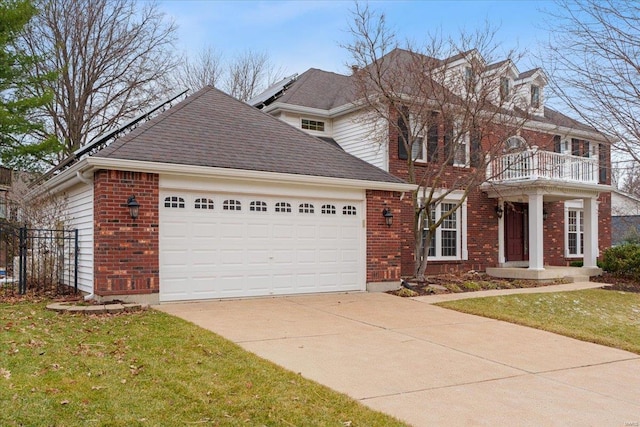 colonial home featuring brick siding, a shingled roof, concrete driveway, a balcony, and a garage