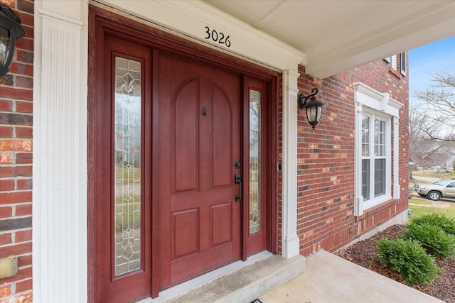 view of exterior entry with a porch and brick siding